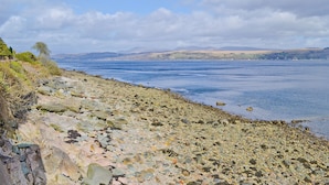 En klippefyldt kystlinje med udsigt til havet og fjerne bakker.
