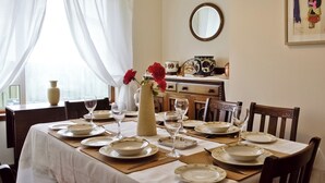 En spisestue med et bord dækket til fire personer, inklusive tallerkener, glas og en vase med blomster.