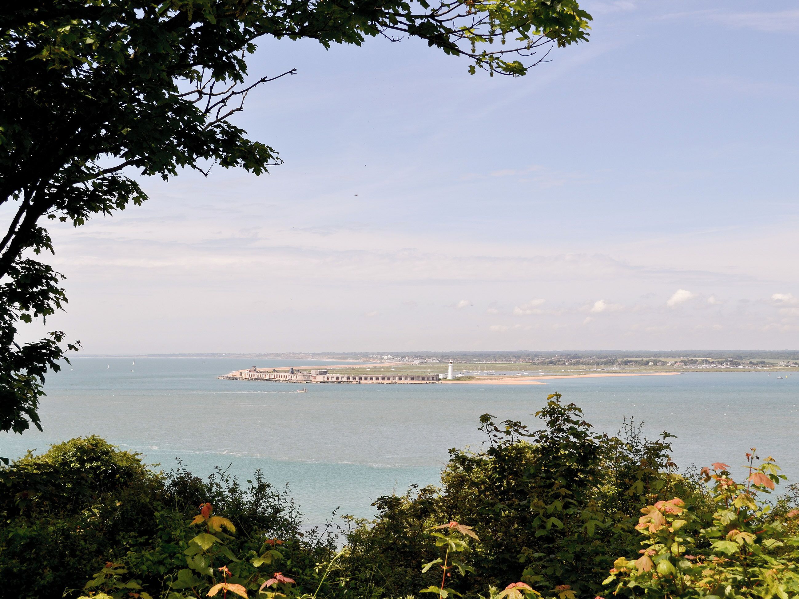 A coastal view with a lighthouse, a pier, and a beach.