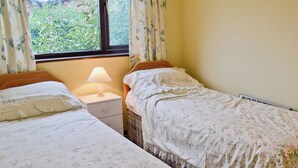 Un dormitorio con dos camas individuales, una mesita de noche con lámpara y una ventana con cortinas.