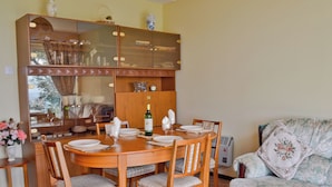 Comedor con una mesa de madera dispuesta para cuatro personas, rodeada de sillas. Encima de la mesa, un aparador grande con puertas de cristal alberga diversos objetos.