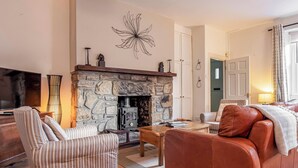 Ein gemütliches Wohnzimmer mit Kamin aus Stein, gestreiften Sesseln, einem Ledersofa und einem Flachbildfernseher.