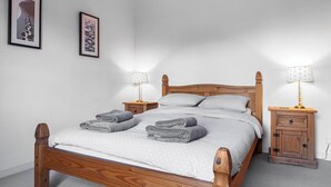 Ein ordentlich bezogenes Bett mit Holz-Kopfstück, zwei Nachttische mit Lampen und zwei gerahmte Bilder an der Wand.