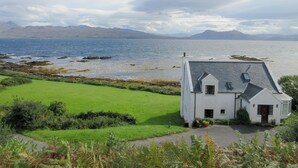 A white house with a sloped roof, a paved driveway, and a grassy lawn. - Macinnisfree Cottage (Saasaig, Teangue, Isle of Skye)
