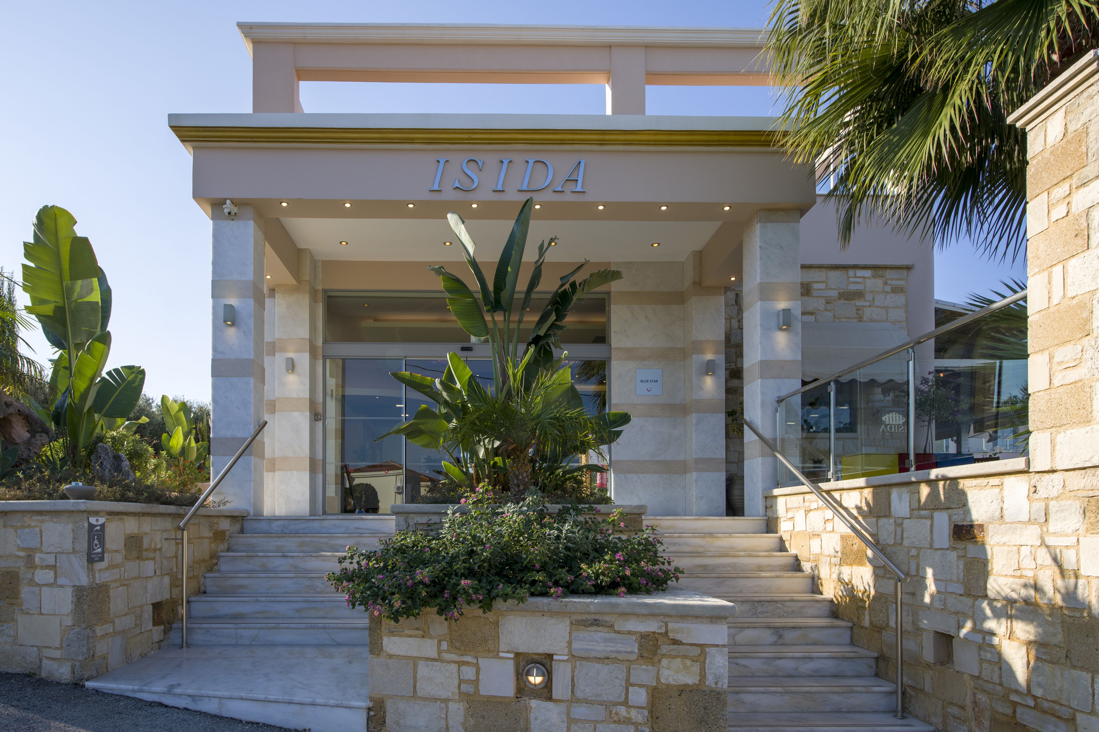 A hotel entrance with a stone facade, a sign reading "ISIDA," and a staircase leading to the entrance.