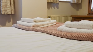 Ein ordentlich bezogenes Bett mit gefalteten weißen Handtüchern, einer rosa gebürsteten Decke und einem Fenster mit Vorhängen.