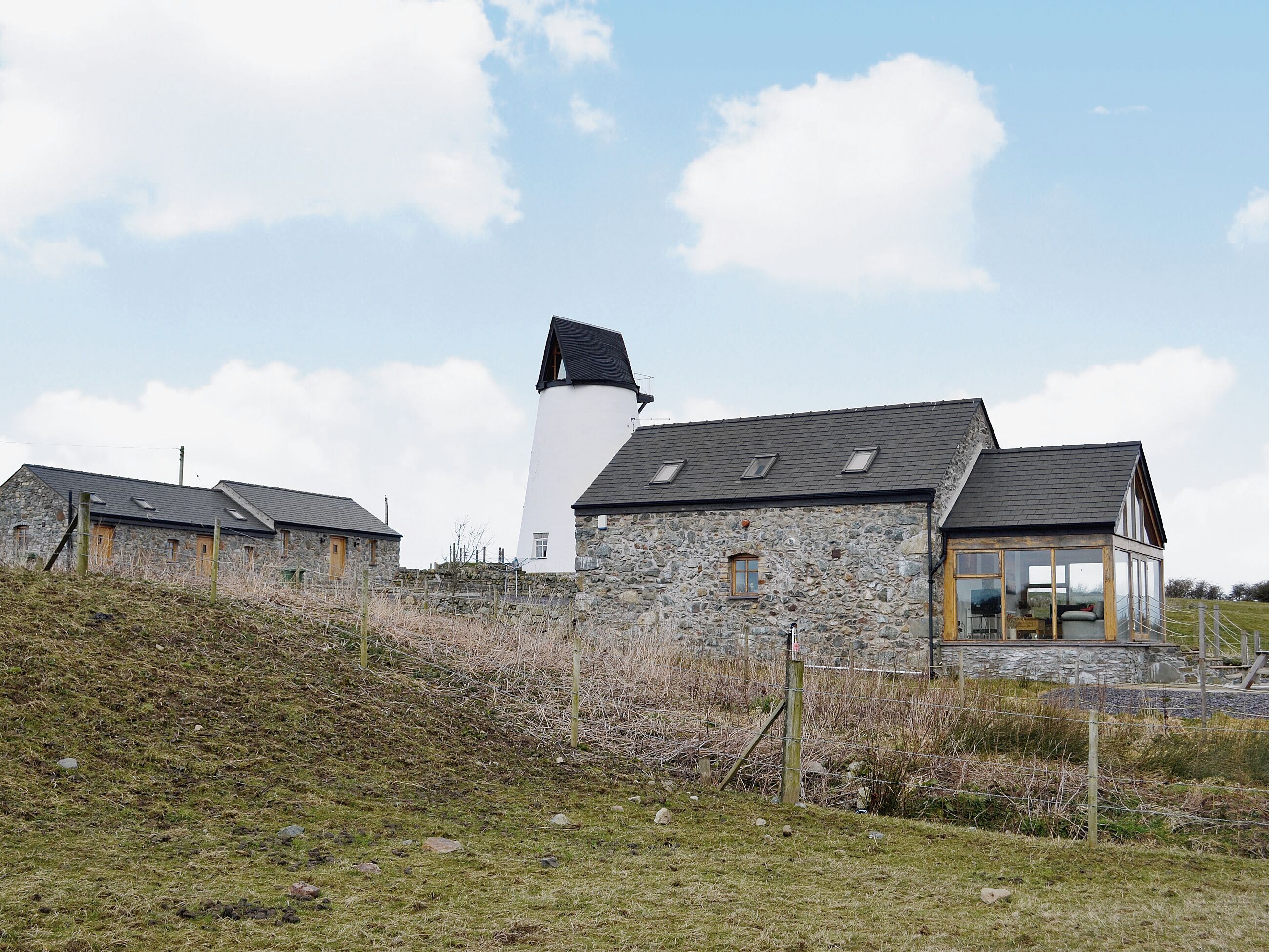 A stone building with a white tower, a wooden structure with a glass enclosure, and a stone wall with a fence.