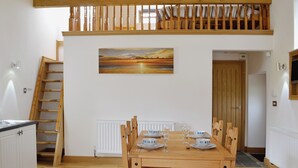 A dining area with a wooden table set for four, a painting above the table, and a wooden staircase to the left. - 2 bedroom accommodation in Tynlon, near Rhosneigr (Tynlon, near Rhosneigr)