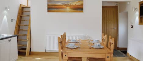Zona pranzo con tavolo in legno apparecchiato per quattro persone, un quadro sopra il tavolo e una scala in legno sulla sinistra.