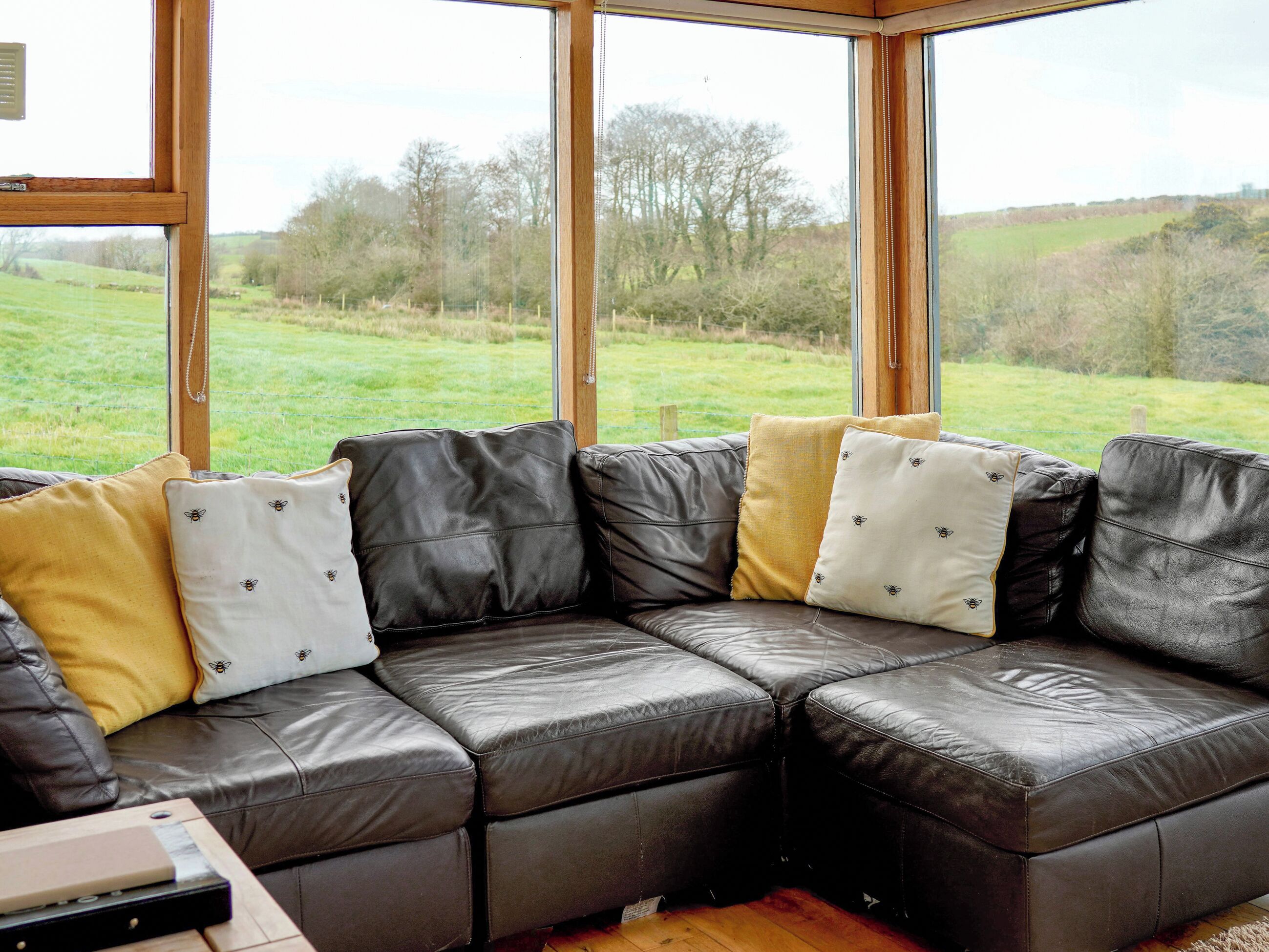 A sectional sofa with multiple cushions, a wooden table, and a view of a grassy field through large windows.