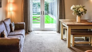 Una habitación con un sofá de cuero marrón, una mesa de madera con un jarrón de flores y un ventanal corredero que da a un área verde exterior.