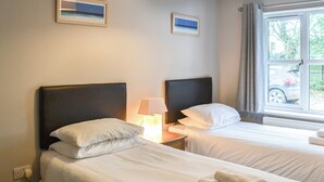 Una habitación de hotel con dos camas individuales, una mesita de noche con lámpara, un ventanal con vistas al exterior y dos cuadros en la pared.