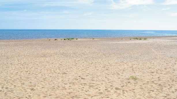 Una playa arenosa con cielo despejado y mar tranquilo.