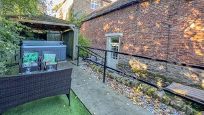 A patio area with outdoor furniture, a hot tub, and a stone wall. - Old Hall Cottage No 1 (Byers Green, near Durham)