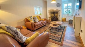 A living room with a brown leather sofa, a round coffee table, a fireplace, and a clock on the wall. - Old Hall Cottage No 1 (Byers Green, near Durham)
