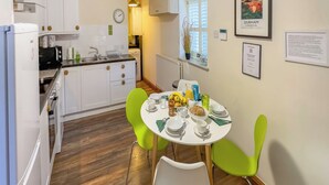 A kitchen with white cabinets, a dining table with green chairs, and a framed picture of Durham. - Old Hall Cottage No 1 (Byers Green, near Durham)
