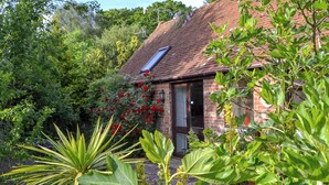 Une maison en briques avec un toit en tuiles, entourée d’une végétation luxuriante et de plantes en fleurs.