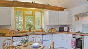 Une cuisine avec des meubles blancs, un plan de travail en bois, une table à manger avec des chaises et une fenêtre avec des stores.