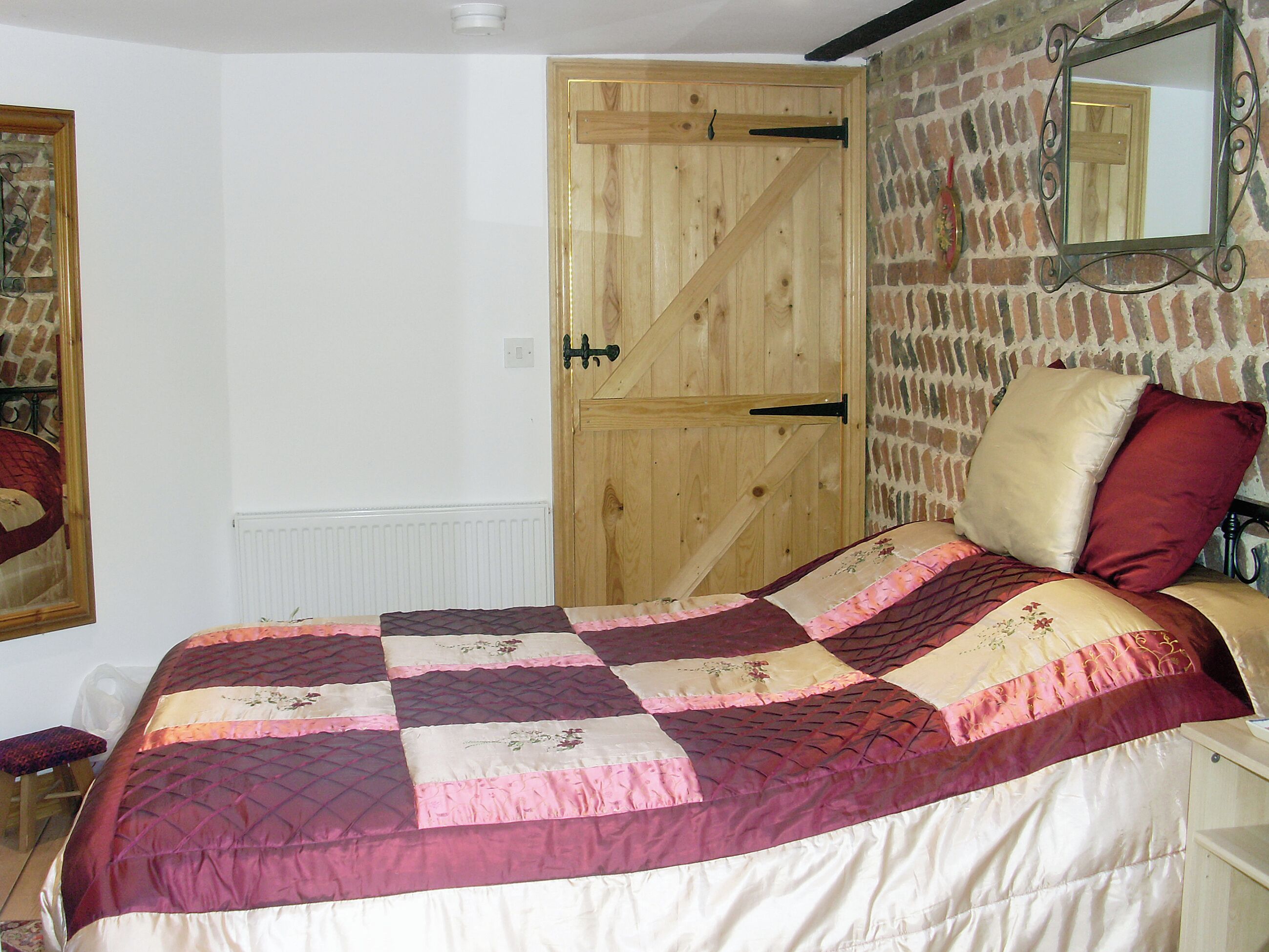 Une chambre avec une porte en bois, une couvre-lit matelassée, un miroir et un mur en briques.