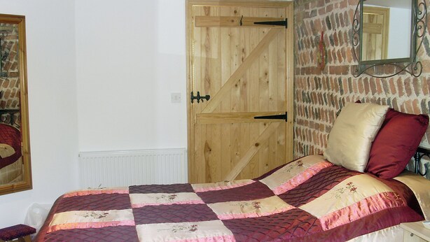 Une chambre avec une porte en bois, une couvre-lit matelassée, un miroir et un mur en briques.