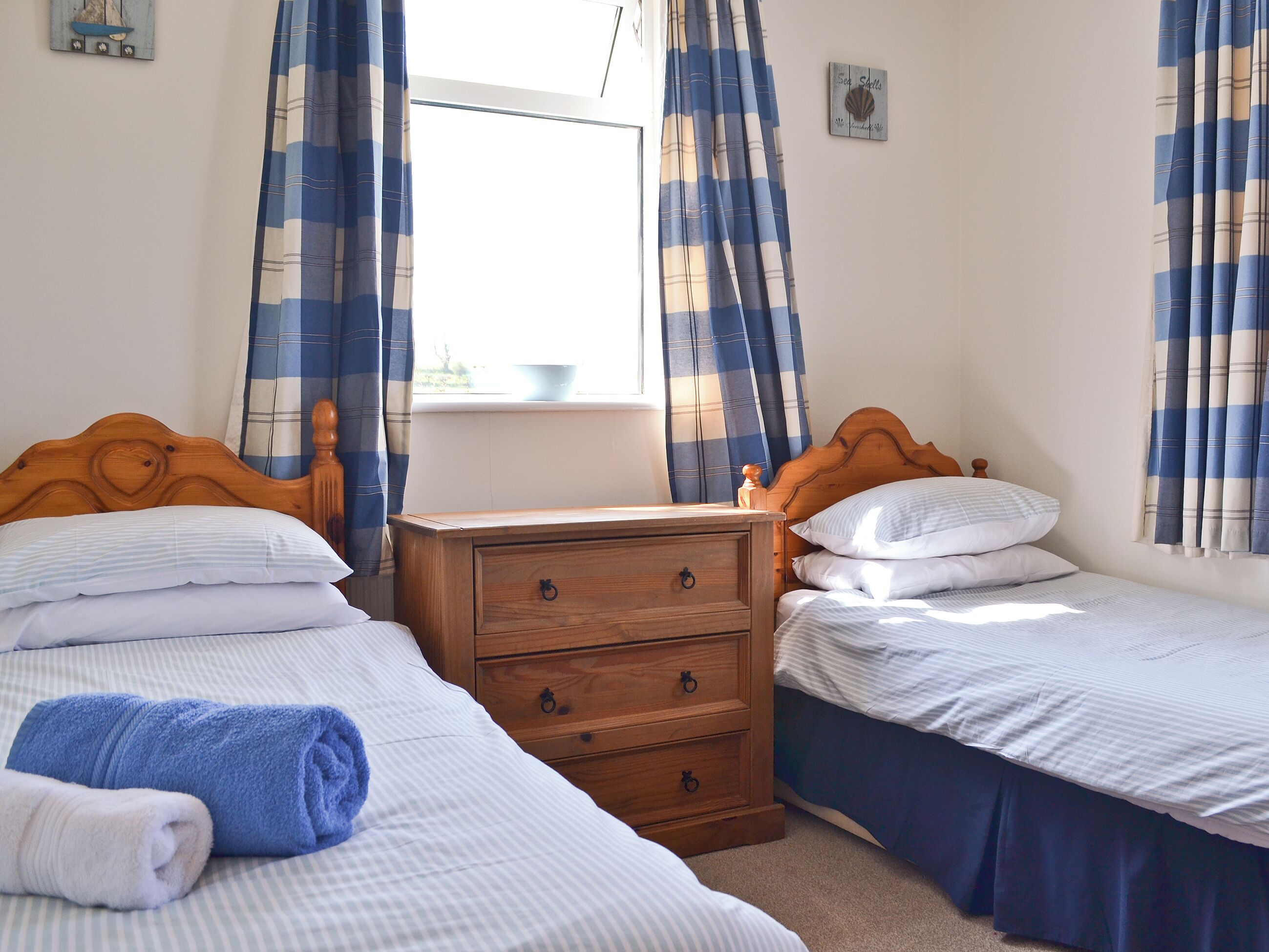 A bedroom with two beds, a wooden dresser, and curtains.
