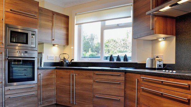 Een moderne keuken met houten kastjes, roestvrijstalen apparatuur en een groot raam dat voor natuurlijk licht zorgt.