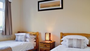 Een hotelkamer met twee eenpersoonsbedden, een nachtkastje met een lamp, een lijst met een foto aan de muur en een raam met gordijnen.