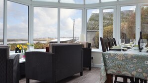 A conservatory with wicker furniture, a table set for dining, and a view of the countryside. - 2 bedroom accommodation in Lower Harrapool, near Broadford (Lower Harrapool, near Broadford)
