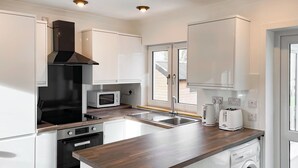 A modern kitchen with white cabinetry, a built-in oven, microwave, and dishwasher, and a wooden countertop. - 2 bedroom accommodation in Lower Harrapool, near Broadford (Lower Harrapool, near Broadford)