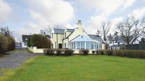 A two-story house with a conservatory, a gravel driveway, and a well-maintained lawn. - 2 bedroom accommodation in Lower Harrapool, near Broadford (Lower Harrapool, near Broadford)