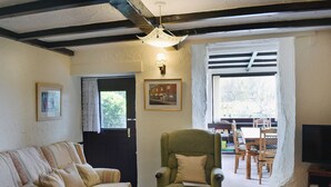 A cozy living room with a sofa, a green armchair, a dining table with chairs, and a television. - Hayrake is in an ideal location, on the fringes of Ambleside. (Ambleside)