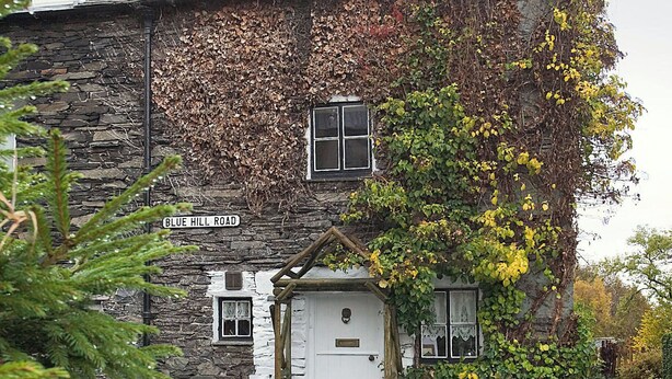 A stone building with a white door and windows, surrounded by ivy and trees. - Hayrake is in an ideal location, on the fringes of Ambleside. (Ambleside)