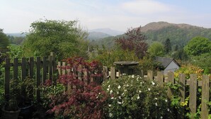 A garden with a wooden fence, various plants, and a view of distant hills. - Hayrake is in an ideal location, on the fringes of Ambleside. (Ambleside)