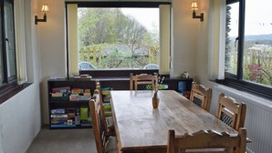 A dining area with a wooden table and chairs, a bookshelf with books, and a view of greenery outside. - Hayrake is in an ideal location, on the fringes of Ambleside. (Ambleside)