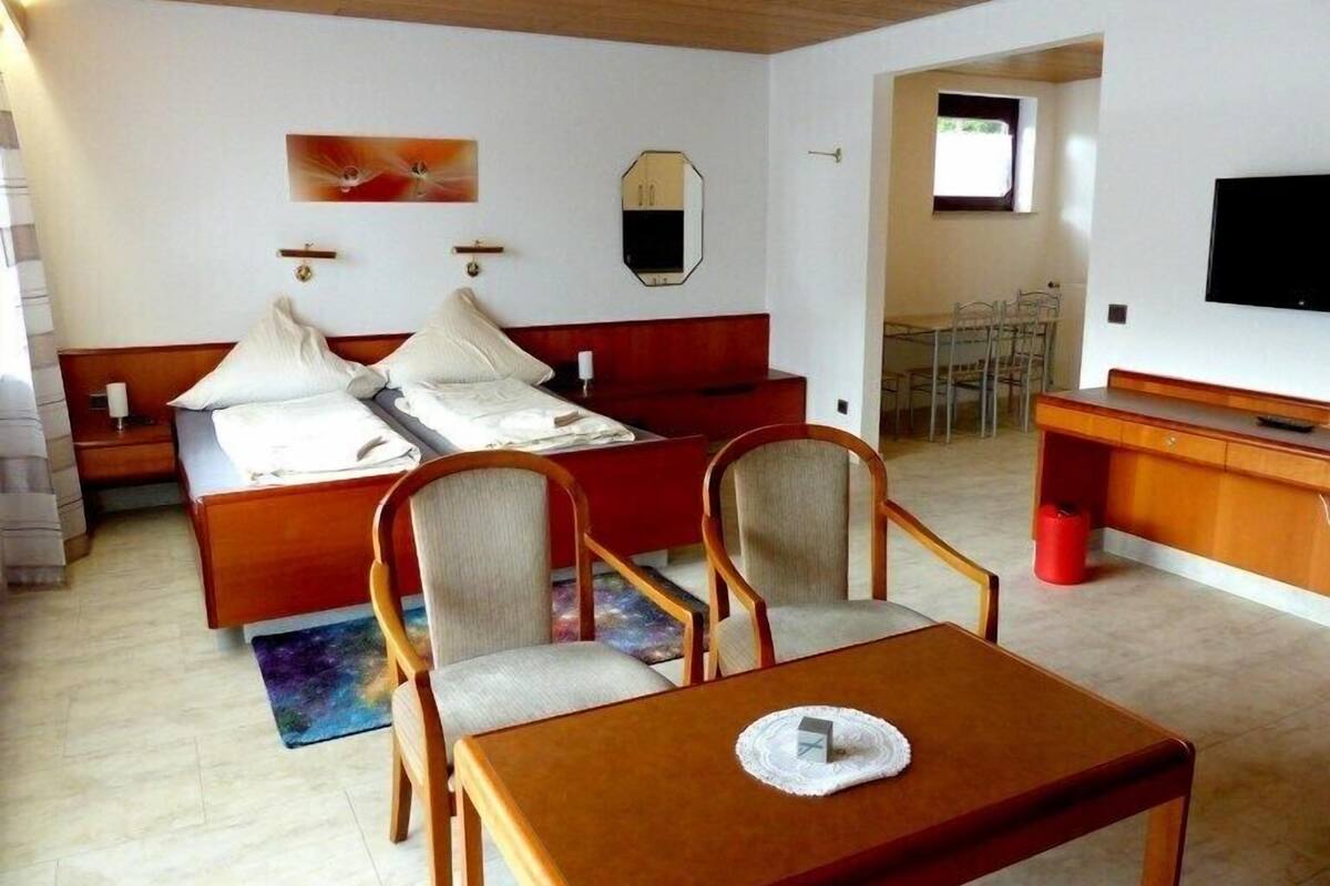 A hotel room with a bed, two chairs, a table, a TV, and a dining area.