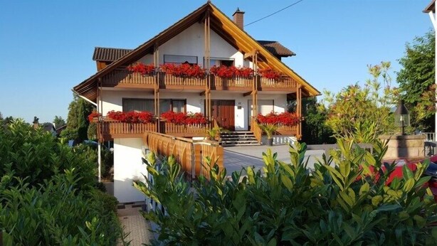 A two-story chalet with a wooden balcony, a front entrance, and a small garden area. - Hotel Garni Sebastian (Kirrweiler)