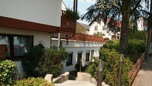 A courtyard with a white building, a wooden fence, and greenery. - Hotel Garni Sebastian (Kirrweiler)