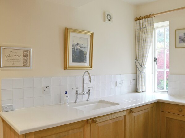 A kitchen with a white countertop, a sink, wooden cabinets, and a window with curtains.