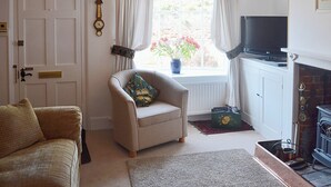 Un salon chaleureux avec un fauteuil beige, un canapé, une télévision, une cheminée et une fenêtre avec des rideaux.