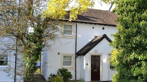 A white two-story house with a dark roof, a front door, and a small porch. - Elm Court 18 has the advantage of being a semi-detached house. (Keswick)