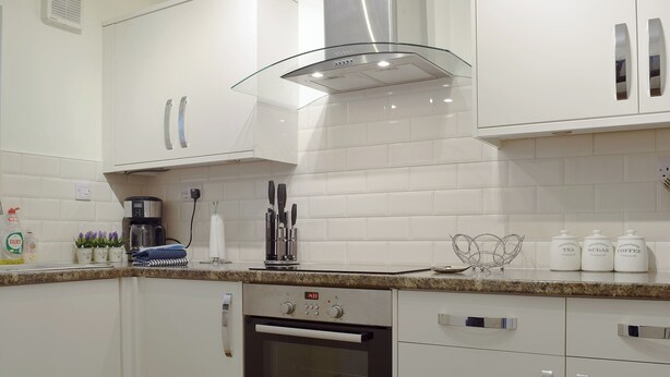 A modern kitchen with white cabinets, a Bosch oven, a coffee maker, and storage jars labeled 'Vintage Pan Sugar Coffee'. - Elm Court 18 has the advantage of being a semi-detached house. (Keswick)