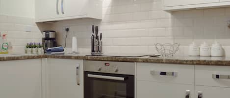 A modern kitchen with white cabinets, a Bosch oven, a coffee maker, and storage jars labeled 'Vintage Pan Sugar Coffee'.