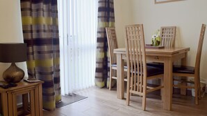 A dining area with a wooden table and chairs, a lamp, and a framed picture on the wall. - Elm Court 18 has the advantage of being a semi-detached house. (Keswick)