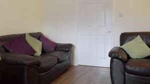 A living room with a brown leather sofa, a white door, and a framed picture on the wall. - Elm Court 18 has the advantage of being a semi-detached house. (Keswick)