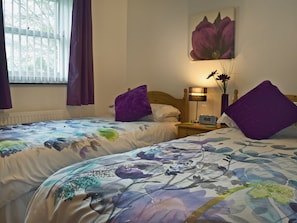 Un dormitorio con dos camas, una mesita de noche con lámpara y una ventana con cortinas.