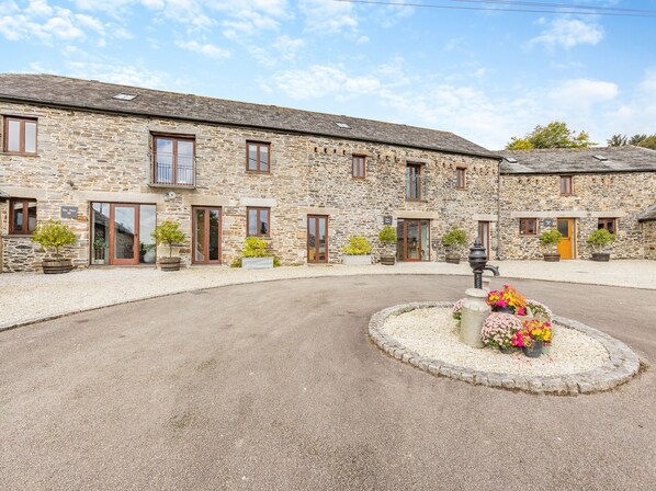 A stone building with multiple windows and doors, a gravel driveway, and a flower bed with various plants.
