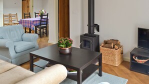 Ein Wohnzimmer mit einer Couch, einem Tisch mit Topfpflanze, einem Kamin, einem Essbereich mit Tisch und Stühlen sowie einem Fernseher.