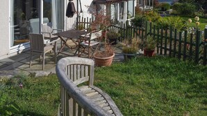 Ein Haus mit einer Terrassenanlage, die Gartenmöbel, einen Holzzaun und Kübelpflanzen zeigt.
