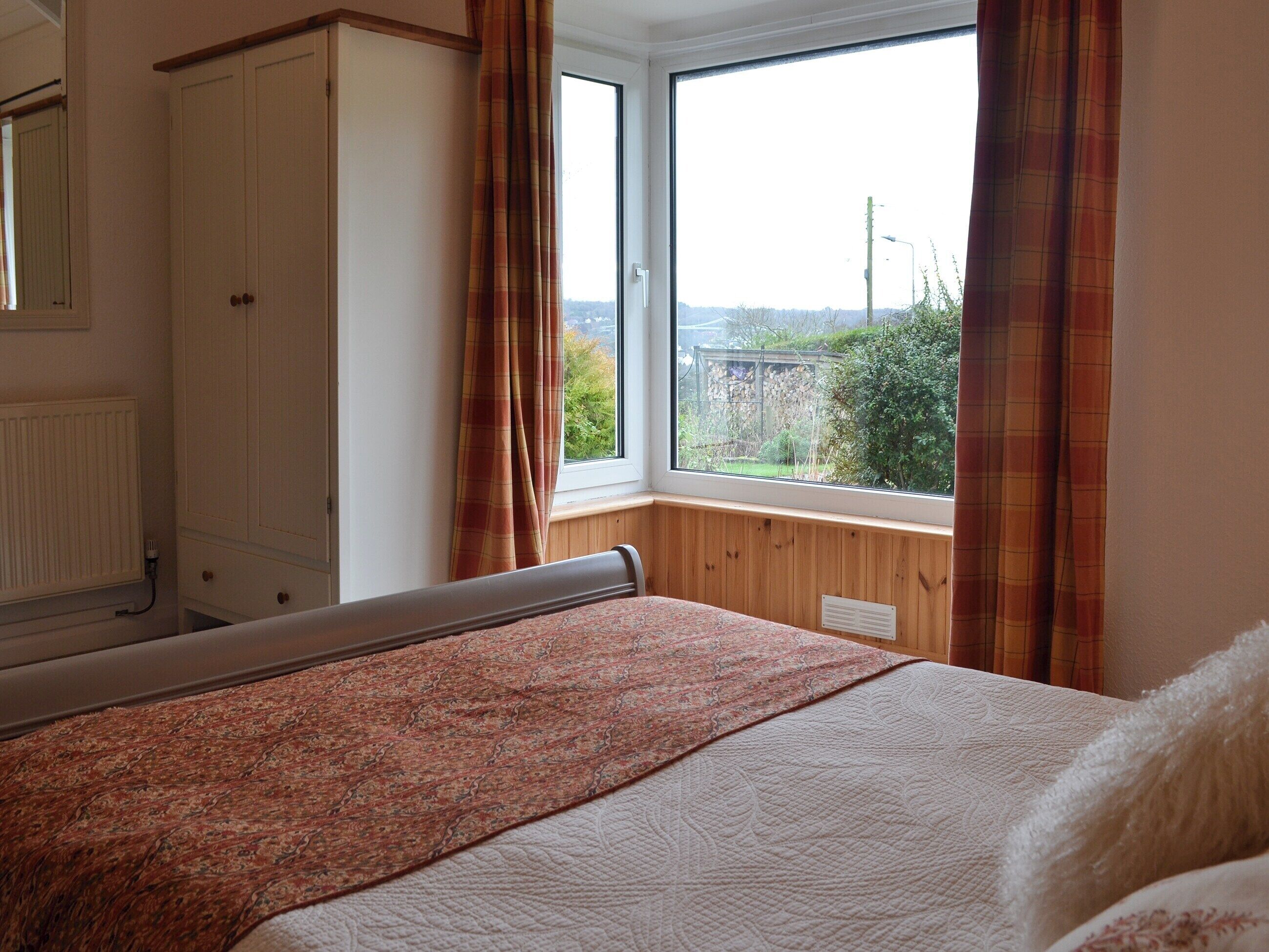 A bedroom with a bed, a window with curtains, a wardrobe, and a radiator.