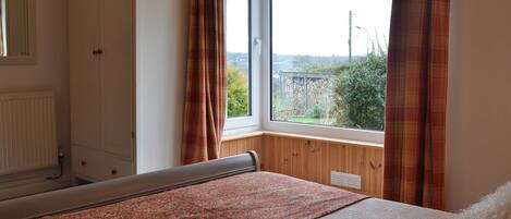 A bedroom with a bed, a window with curtains, a wardrobe, and a radiator.